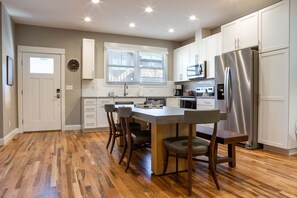 A modern kitchen with a central island, white cabinetry, stainless steel appliances, and a hardwood floor. - The Fold at Reynolds Mountain | Asheville 10 Townhomes, Hot Tubs, Sleeps 80 (Asheville)
