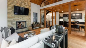 A spacious living area with a fireplace, a sofa, and a dining table. - Balsam Mountain Tree House | Luxury Retreat | Golf & Exclusive Club Amenities (Sylva)