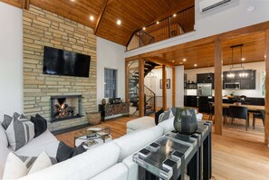A spacious living area with a fireplace, a sofa, and a dining table. - Balsam Mountain Tree House | Luxury Retreat | Golf & Exclusive Club Amenities (Sylva)