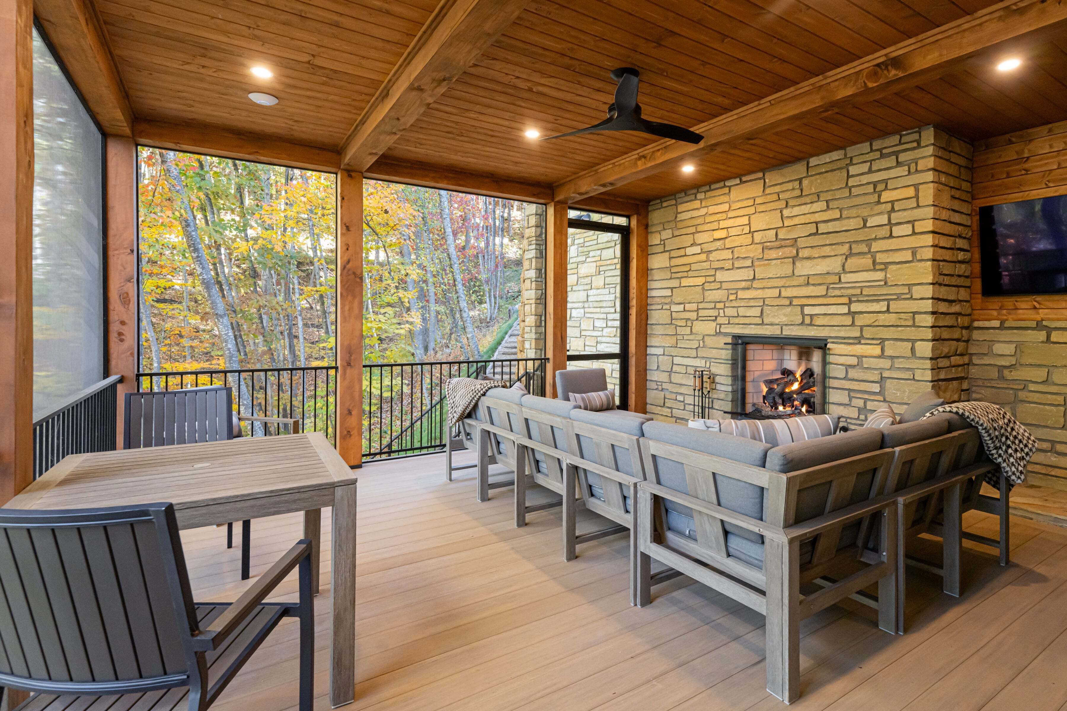 A wooden deck with a stone fireplace, seating area, and a television mounted on the wall.