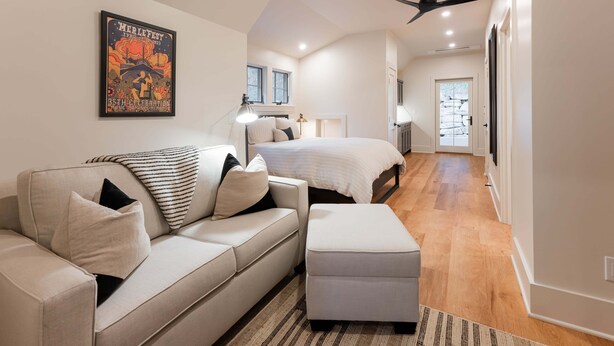 A modern bedroom with a bed, a sofa, and a ceiling fan. - Balsam Mountain Tree House | Luxury Retreat | Golf & Exclusive Club Amenities (Sylva)