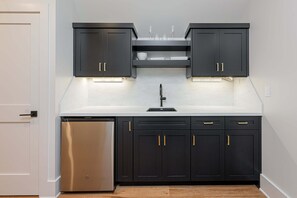 A modern kitchen with dark cabinetry, a stainless steel refrigerator, and under-cabinet lighting. - Balsam Mountain Tree House | Luxury Retreat | Golf & Exclusive Club Amenities (Sylva)
