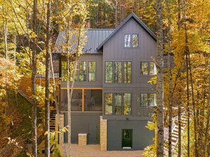 A modern two-story house with multiple windows, surrounded by trees. - Balsam Mountain Tree House | Luxury Retreat | Golf & Exclusive Club Amenities (Sylva)