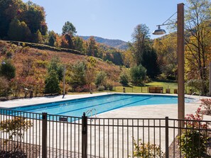 Une piscine fermée, entourée d’une clôture, avec en arrière-plan des arbres et des collines aux couleurs automnales.