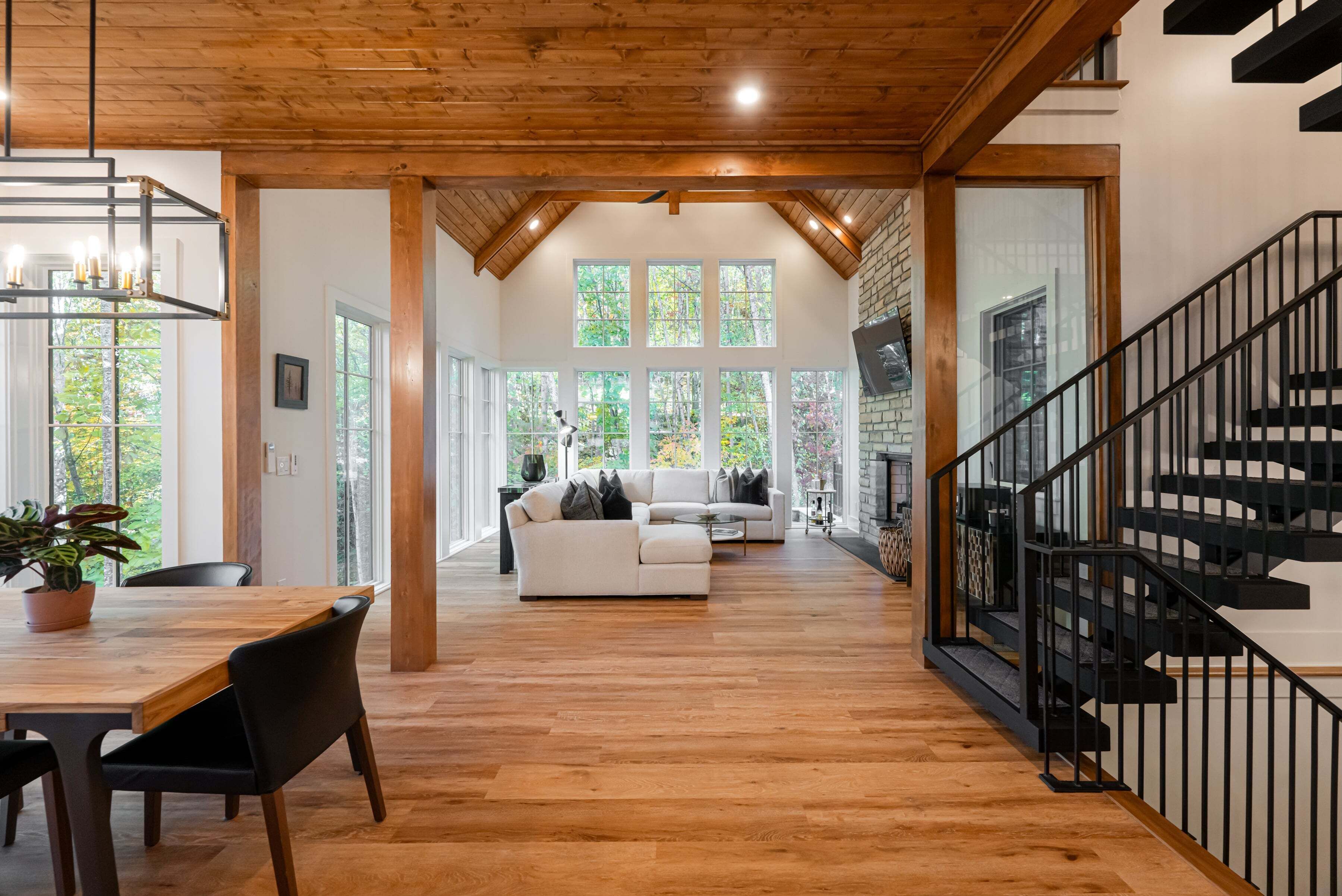 Amplia sala de estar con piso de madera, un sofá blanco y una escalera con barandillas negras.