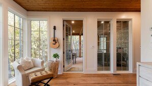A spacious room with a wooden floor, a white sofa, a coffee table, and a guitar on the wall. - Balsam Mountain Tree House | Luxury Retreat | Golf & Exclusive Club Amenities (Sylva)