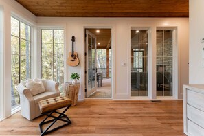 A spacious room with a wooden floor, a white sofa, a coffee table, and a guitar on the wall. - Balsam Mountain Tree House | Luxury Retreat | Golf & Exclusive Club Amenities (Sylva)