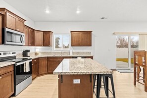 Eine moderne Küche mit Granit Arbeitsplatten, Holzschränken, einem Edelstahlbackofen und einer großen Kücheninsel mit Barhocker.