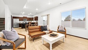 A spacious living area with a sofa, chairs, and a coffee table. A kitchen with modern appliances is visible in the background. - Cheney Home | Close to Interstate & Airport (Cheney)