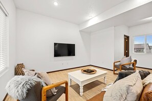 A modern living room with a flat-screen TV, wooden furniture, and a white coffee table. - Cheney Home | Close to Interstate & Airport (Cheney)