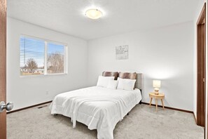 Ein Schlafzimmer mit Bett, Nachttisch, Fenster und Deckenleuchte.