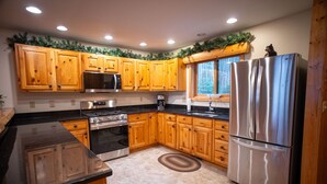 A kitchen with wooden cabinets, stainless steel appliances, a window with a view, and a decorative garland. - The "Grand Dame" of Timber Bay (Babbitt)