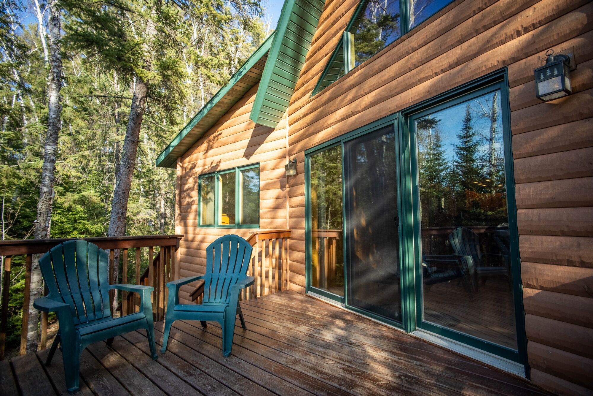 Een houten chalet met een terras, twee stoelen en een grote schuifdeur van glas.