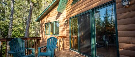 Een houten chalet met een terras, twee stoelen en een grote schuifdeur van glas.