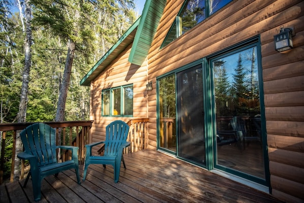 A wooden cabin with a deck, two chairs, and a large sliding glass door.