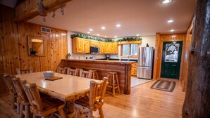 A wooden cabin interior with a dining area, kitchen, and a door with a decorative glass panel. - The "Grand Dame" of Timber Bay (Babbitt)