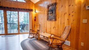 Een houten interieur met een schommelstoel, een bank en een open haard.