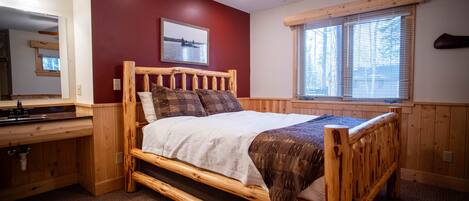 A wooden bed with a headboard, a window with blinds, a ceiling fan, and a framed picture on the wall.
