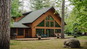 Eine Blockhütte mit einer großen Veranda, vielen Fenstern und einem Kamin aus Stein.