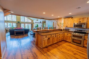 A spacious kitchen with wooden cabinets, a dining area with a table and chairs, and a living room with a sofa and piano. - Ultimate Group Getaway. Luxury Private Lodge Sleeps 15. CB 15. (Babbitt)