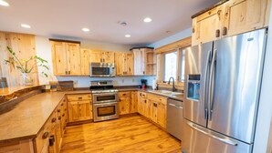 A modern kitchen with wooden cabinets, stainless steel appliances, and a wooden floor. - The exclusive "Owner’s Edition": The Hefty Logger Lodge (Babbitt)