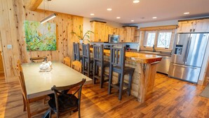 A wooden-paneled kitchen with a dining area, stainless steel appliances, and a large window. - The exclusive "Owner’s Edition": The Hefty Logger Lodge (Babbitt)