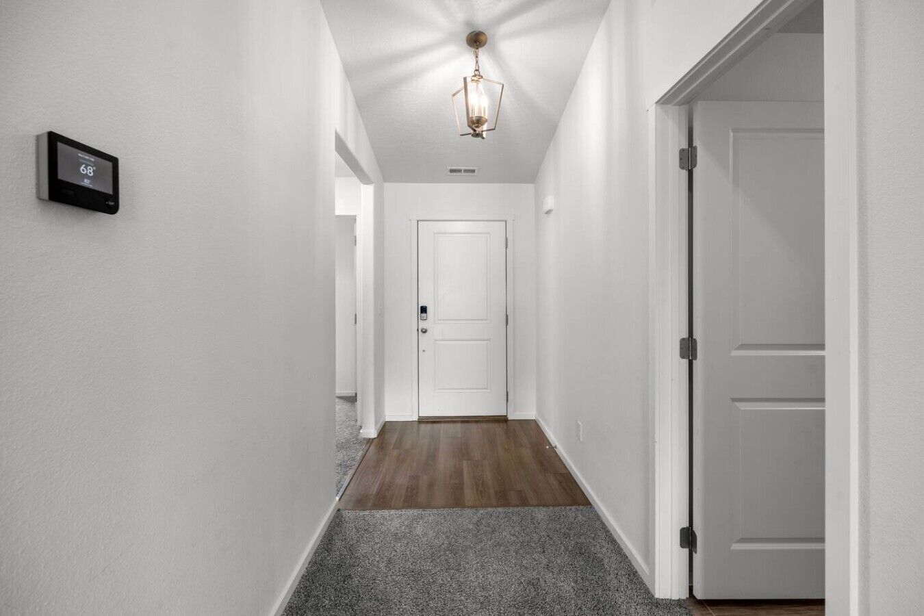 A hallway with a thermostat, a door, and a ceiling light fixture.