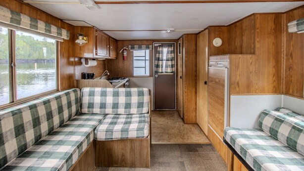Een compact camperinterieur met een kitchenette, een zithoek met geruit kussens en een deur naar buiten.
