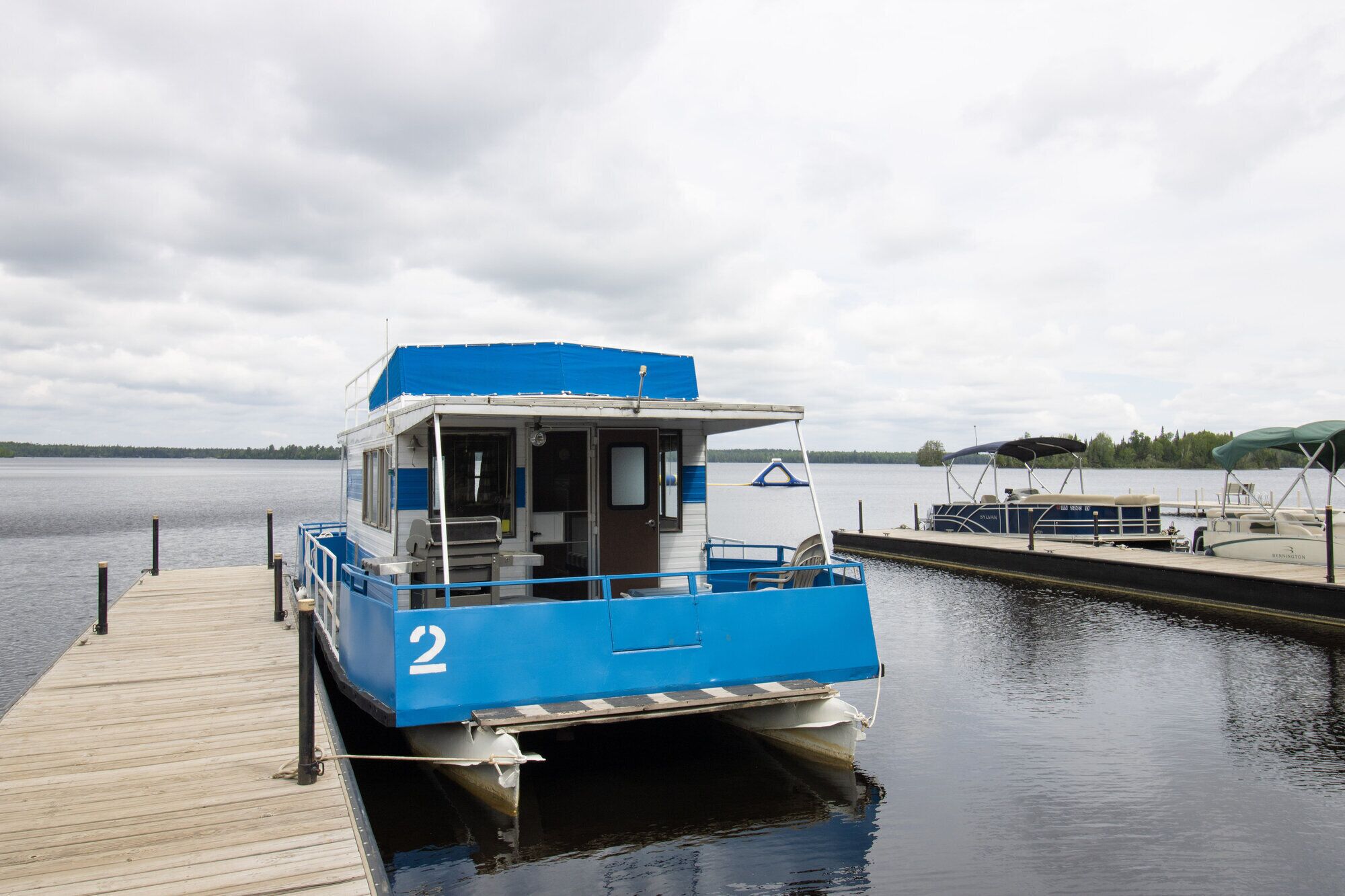 A blue and white boat docked at a pier with a calm lake in the background.