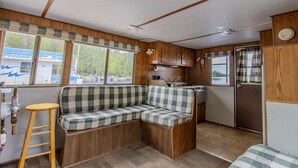 Een compact camperinterieur met een kitchenette, een zithoek met een geruit bankje en een klein krukje.