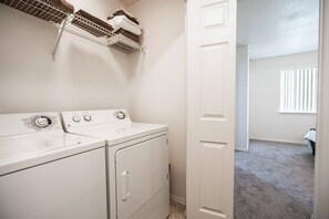 Un lavadero con dos lavadoras blancas, un tendedero y una puerta que da a otra habitación.