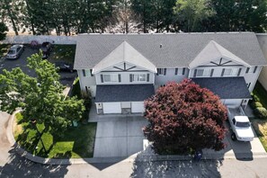 Ein zweistöckiges Wohngebäude mit Garage, Auffahrt und einem großen Baum davor.
