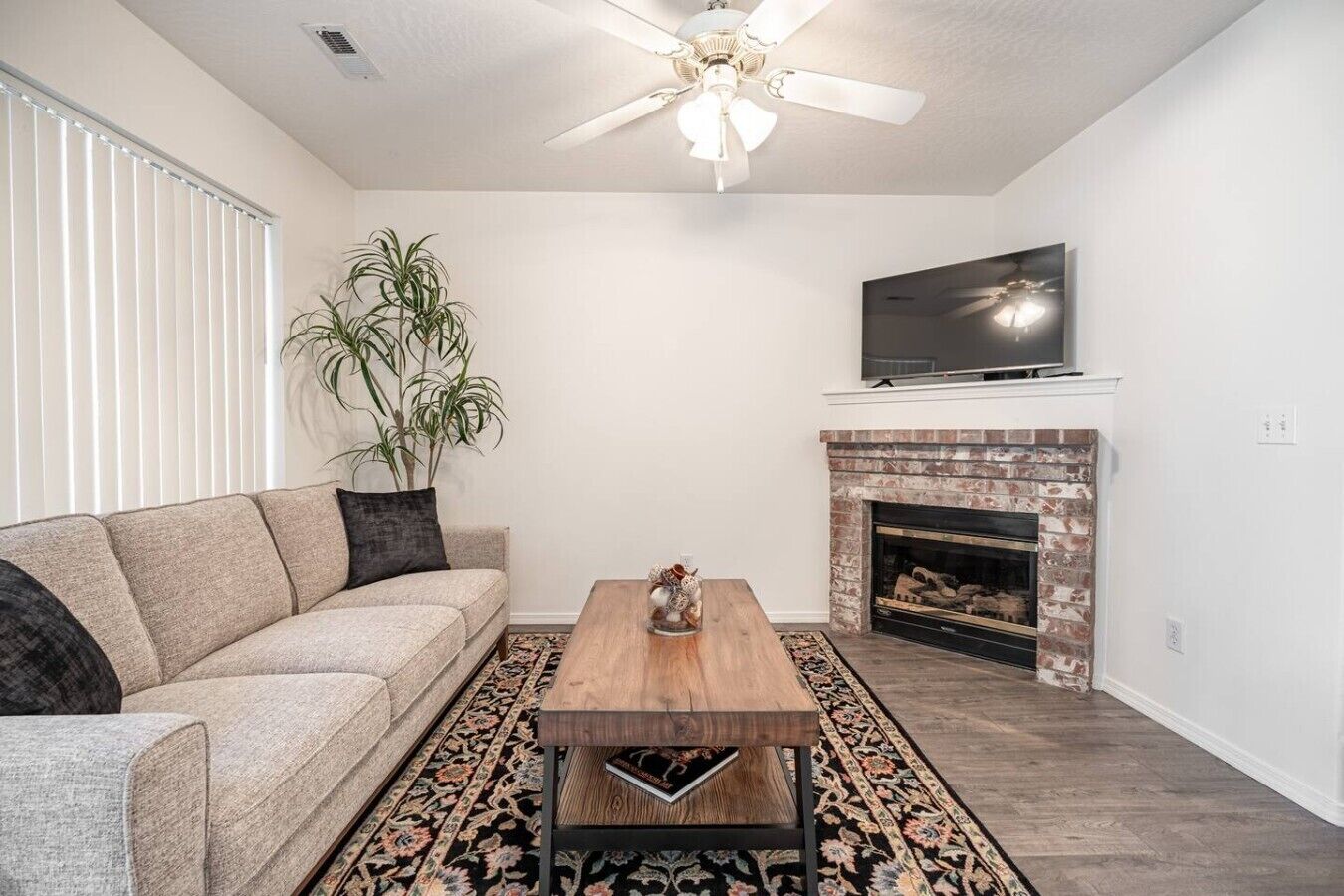 A living room with a sofa, coffee table, fireplace, TV, and ceiling fan.
