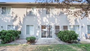 A two-story residential building with a front entrance, a covered porch, and two small front yard bushes. - Cozy Coeur d’Alene Townhome (Coeur d`Alene)