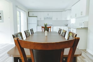 A modern kitchen with white cabinets, a dining table with chairs, and a potted plant. - Leo Cottage - 5-Bedroom Cottage – Family Friendly (Trent Lakes)