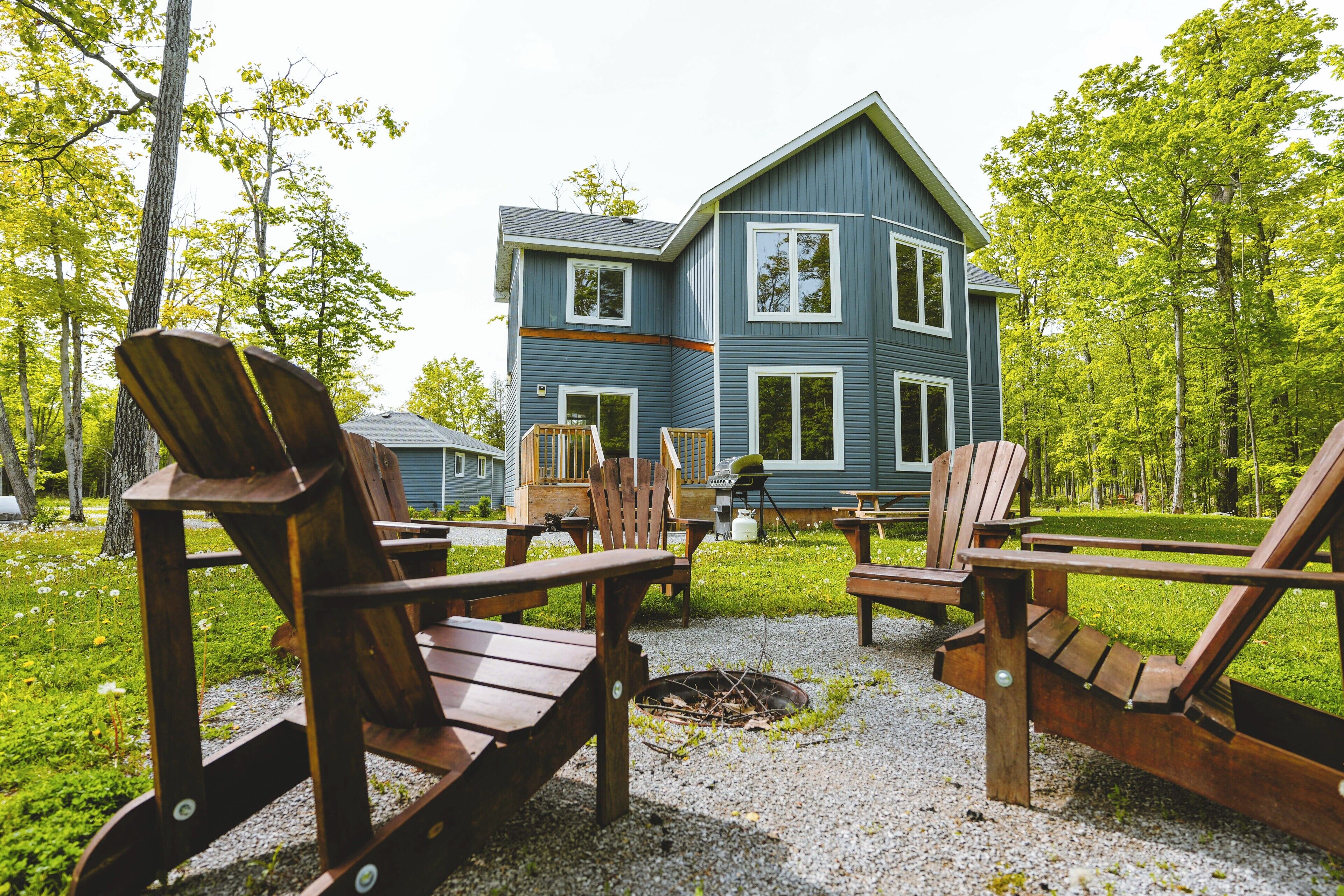 A two-story house with a deck, surrounded by trees and outdoor seating.