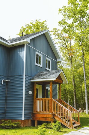 A two-story house with a wooden porch and a staircase leading to the entrance. - Leo Cottage - 5-Bedroom Cottage – Family Friendly (Trent Lakes)