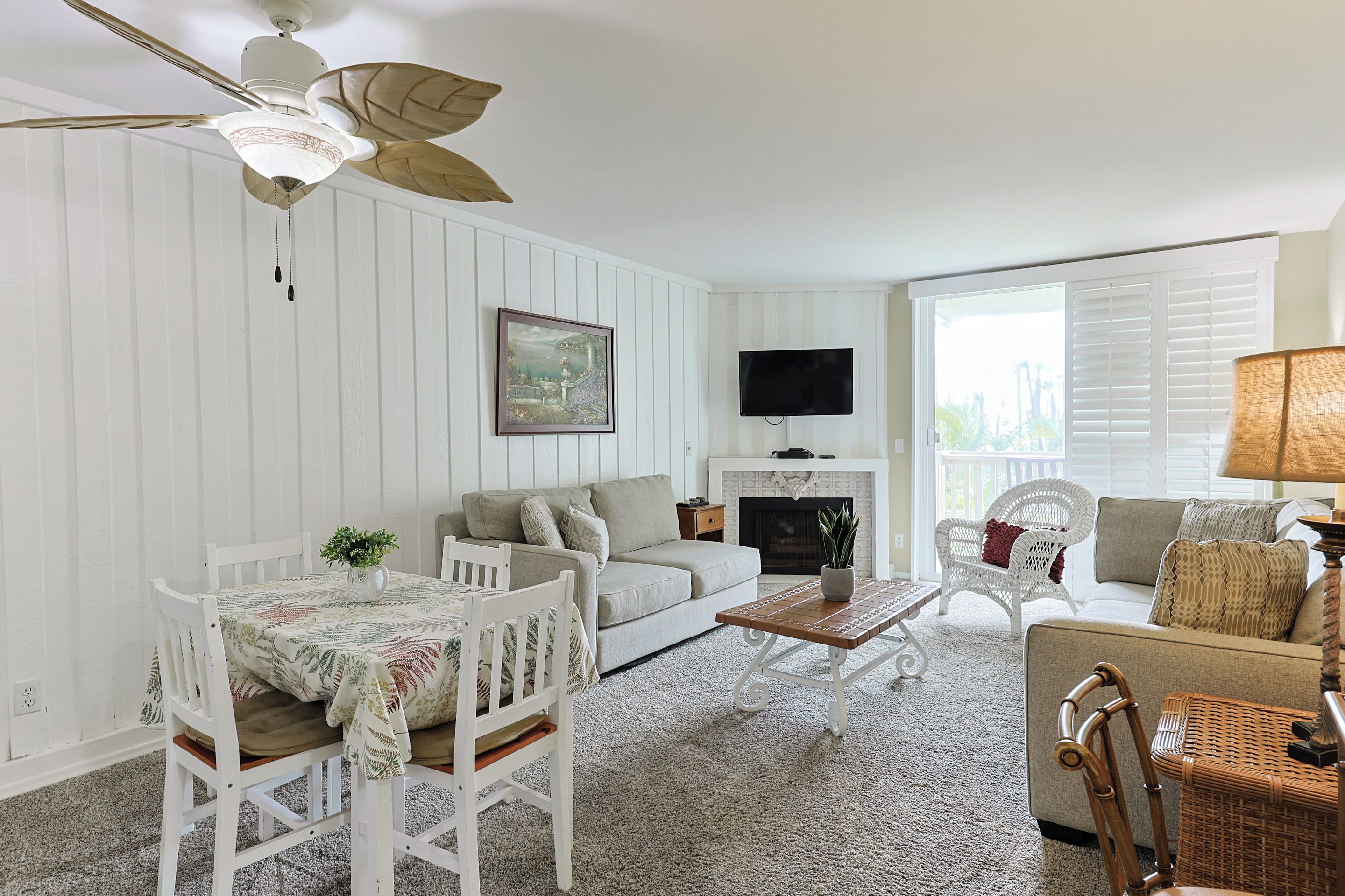 A living room with a white sofa, a dining table with chairs, a fireplace, and a television mounted on the wall.