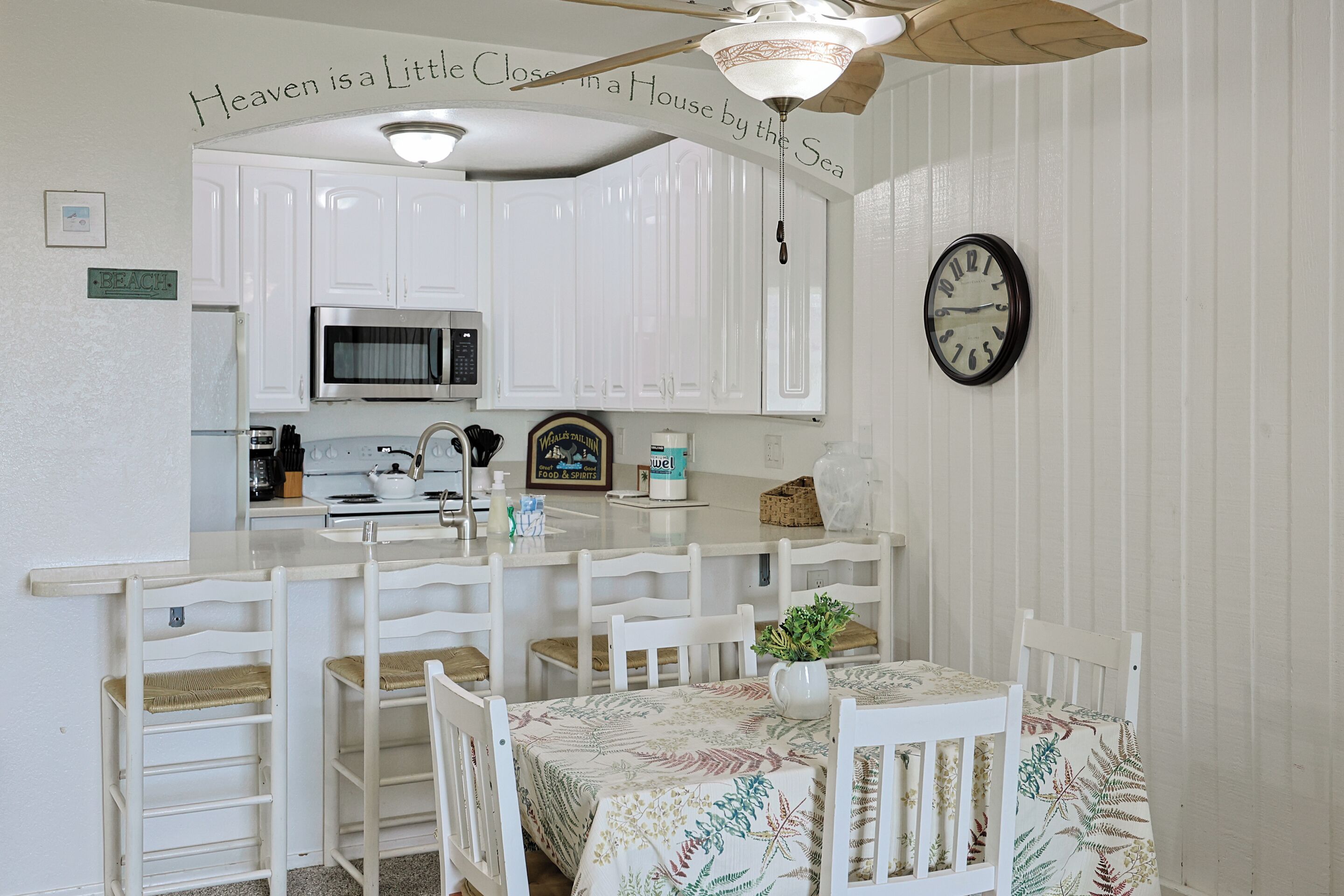 A kitchen with white cabinets, a microwave, and a clock on the wall.