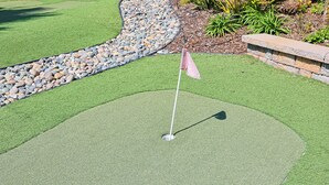 A golf putting green with a flagstick, surrounded by a stone border and a pebble bed. - Whispering Waters: A Tranquil One-bedroom Retreat With Peek Ocean Views (Oceanside)
