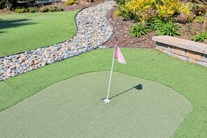 A golf putting green with a flagstick, surrounded by a stone border and a pebble bed. - Whispering Waters: A Tranquil One-bedroom Retreat With Peek Ocean Views (Oceanside)