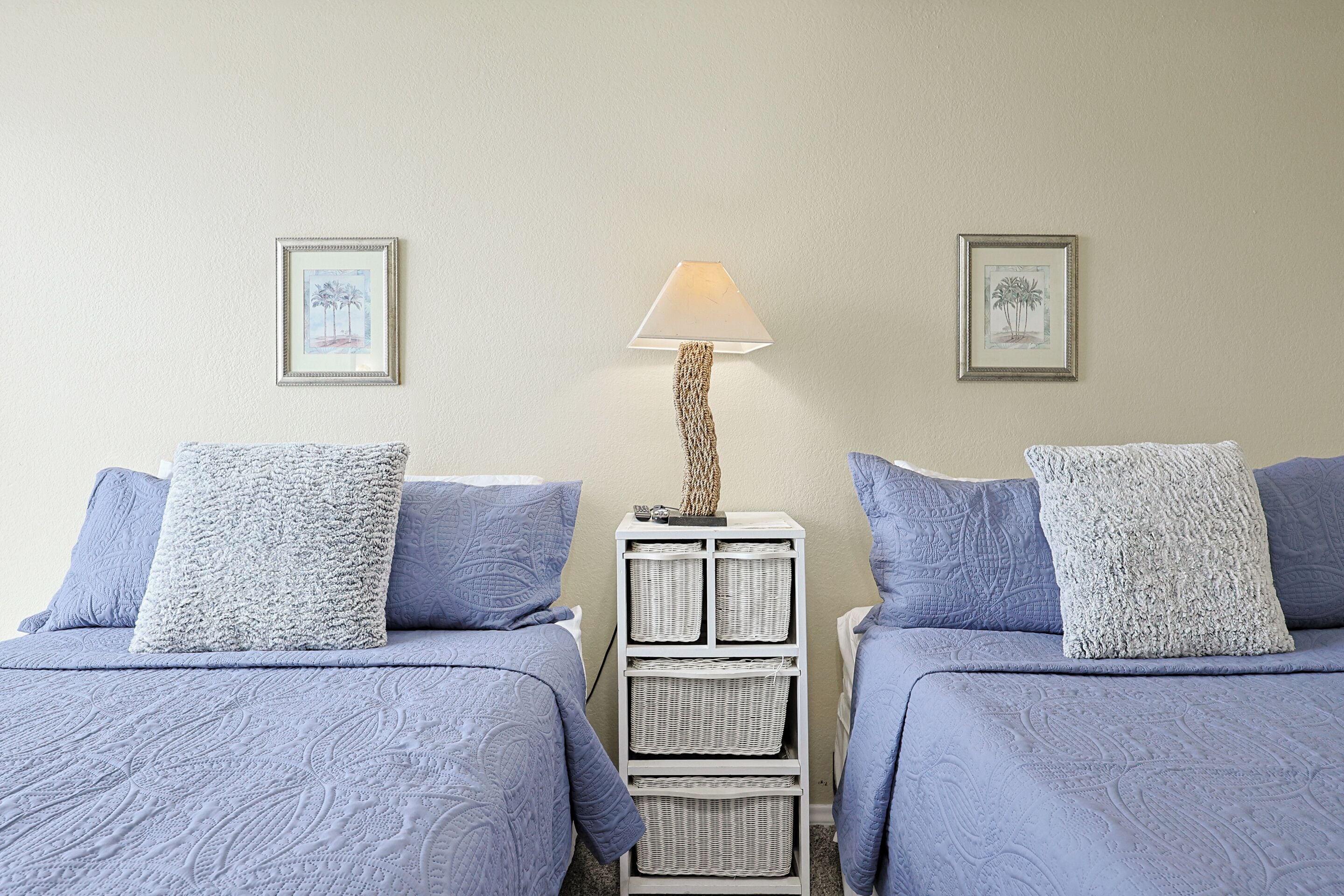A room with two beds, a nightstand with a lamp, and framed pictures on the wall.