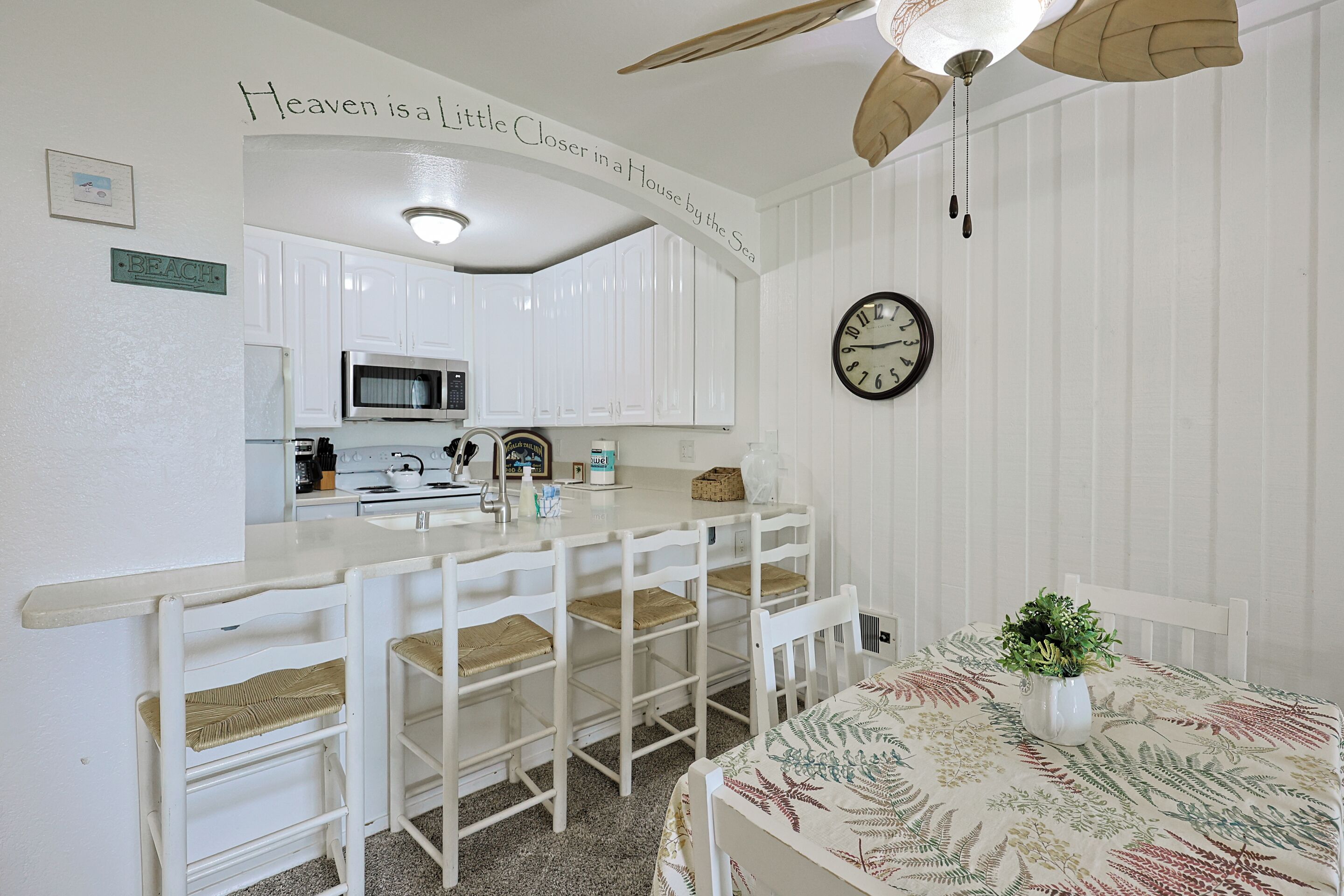 A kitchen with white cabinets, a microwave, a clock, and a ceiling fan.