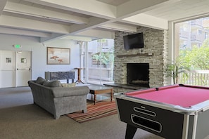 A pool table, a sofa, a fireplace, and a TV in a modern lounge area. - Whispering Waters (Oceanside)