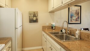 Eine Küche mit weißen Schränken, einer Granit-Arbeitsplatte, einer Edelstahl-Spüle und einem Kühlschrank.