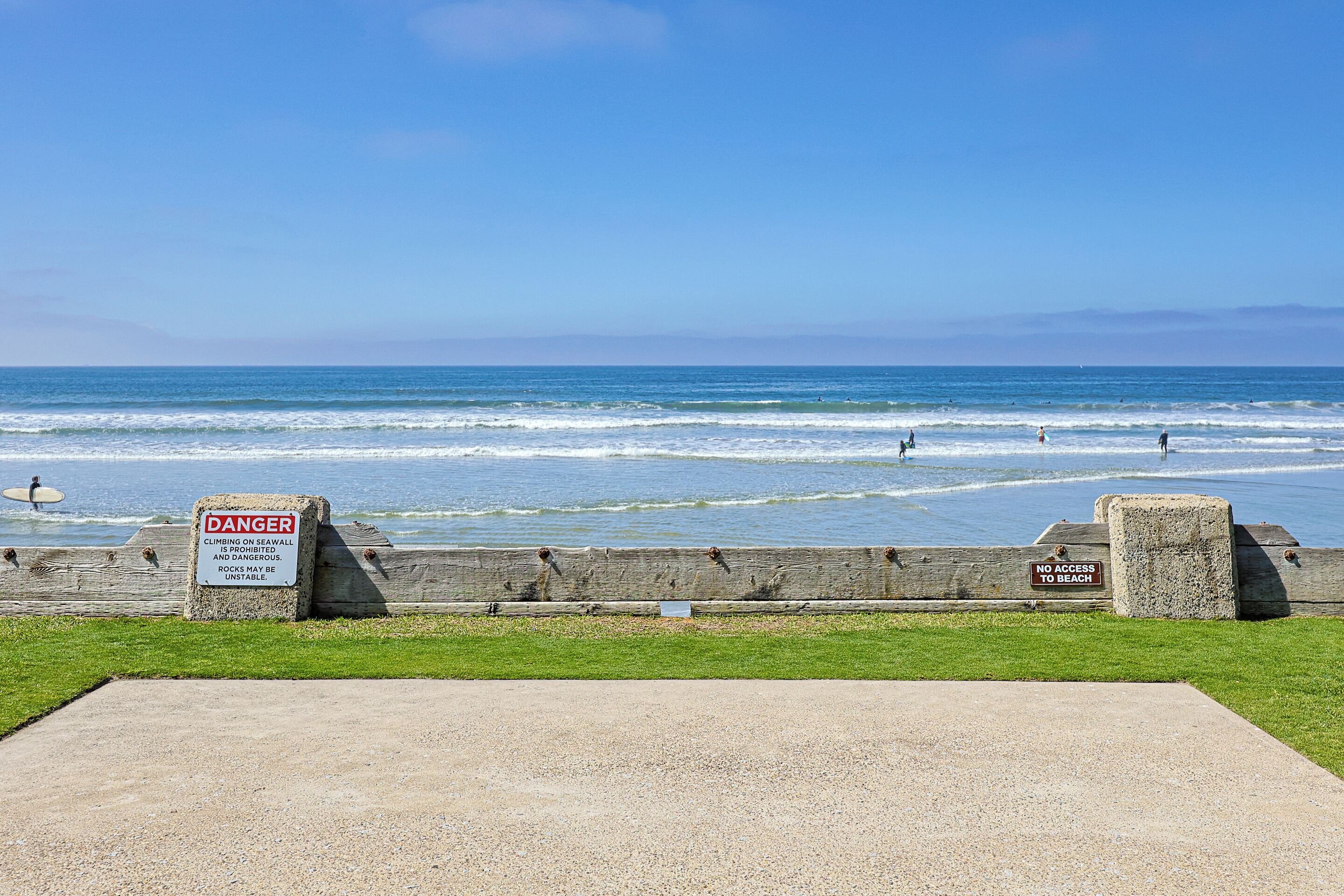 A beach with warning signs, a wooden barrier, and a clear blue sky.