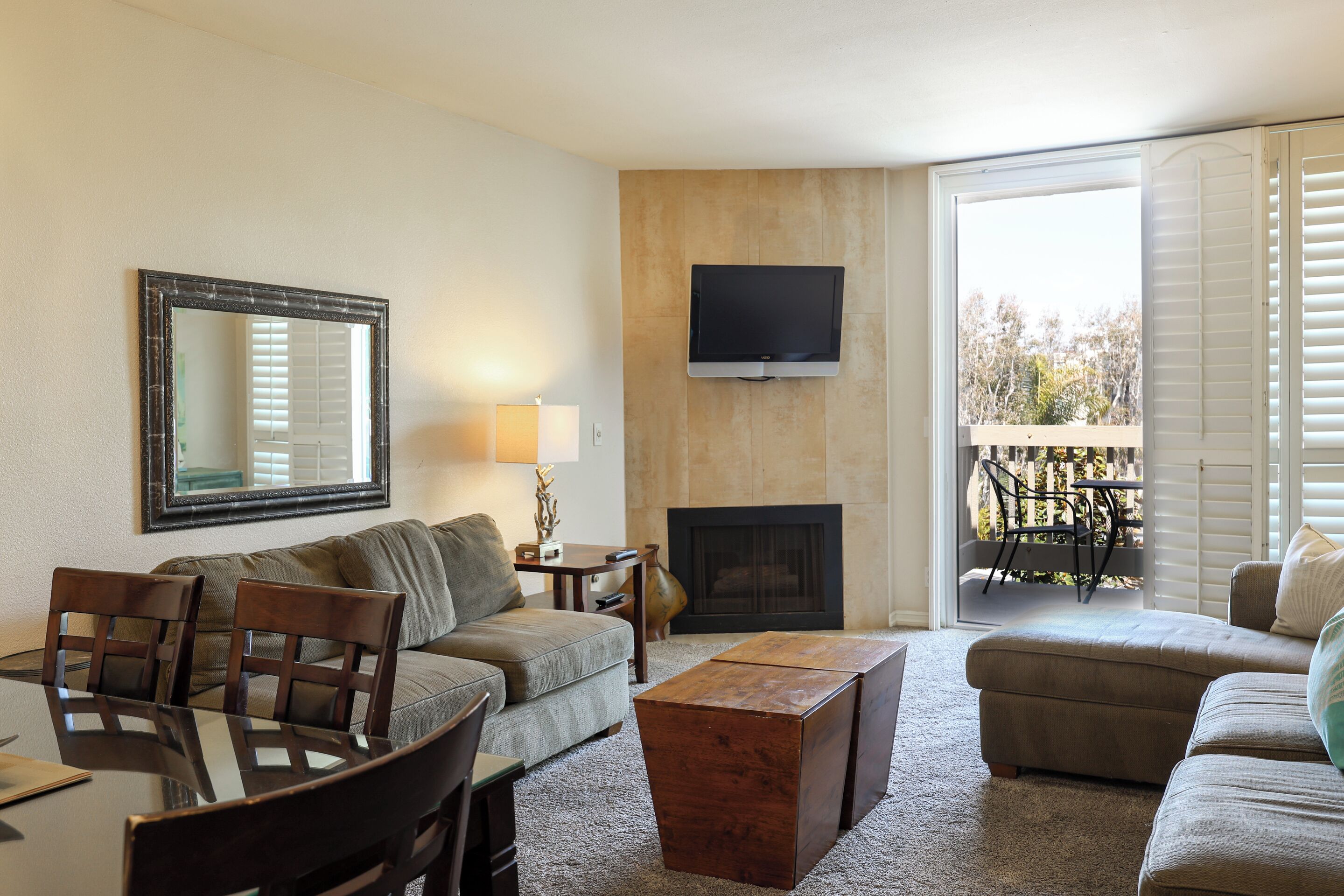 A living room with a sofa, chairs, a coffee table, a TV, a fireplace, and a balcony with outdoor furniture.
