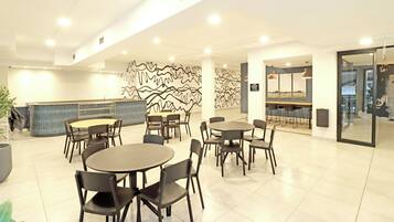A modern hotel lobby with round tables and chairs, a reception desk, and a decorative wall.