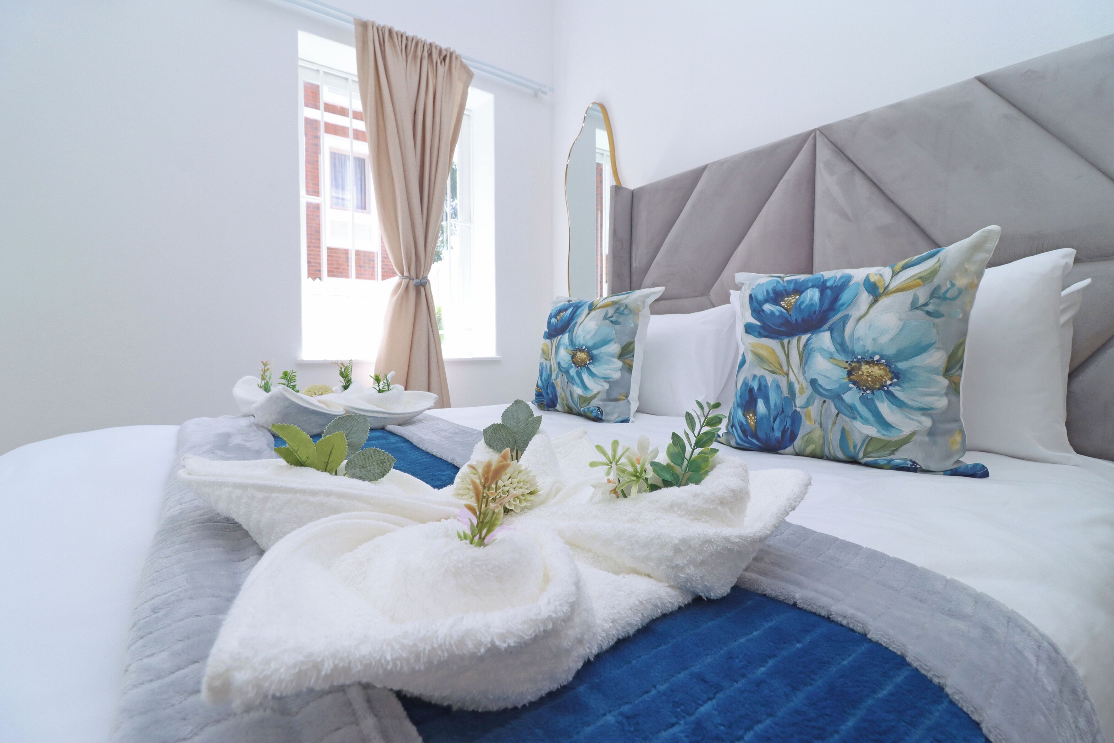 A neatly arranged hotel room with a bed, pillows, a bedside table, and a window with curtains.