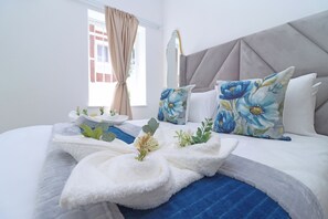 Ein ordentlich eingerichtetes Hotelzimmer mit einem Bett, Kissen, einem Nachttisch und einem Fenster mit Vorhängen.